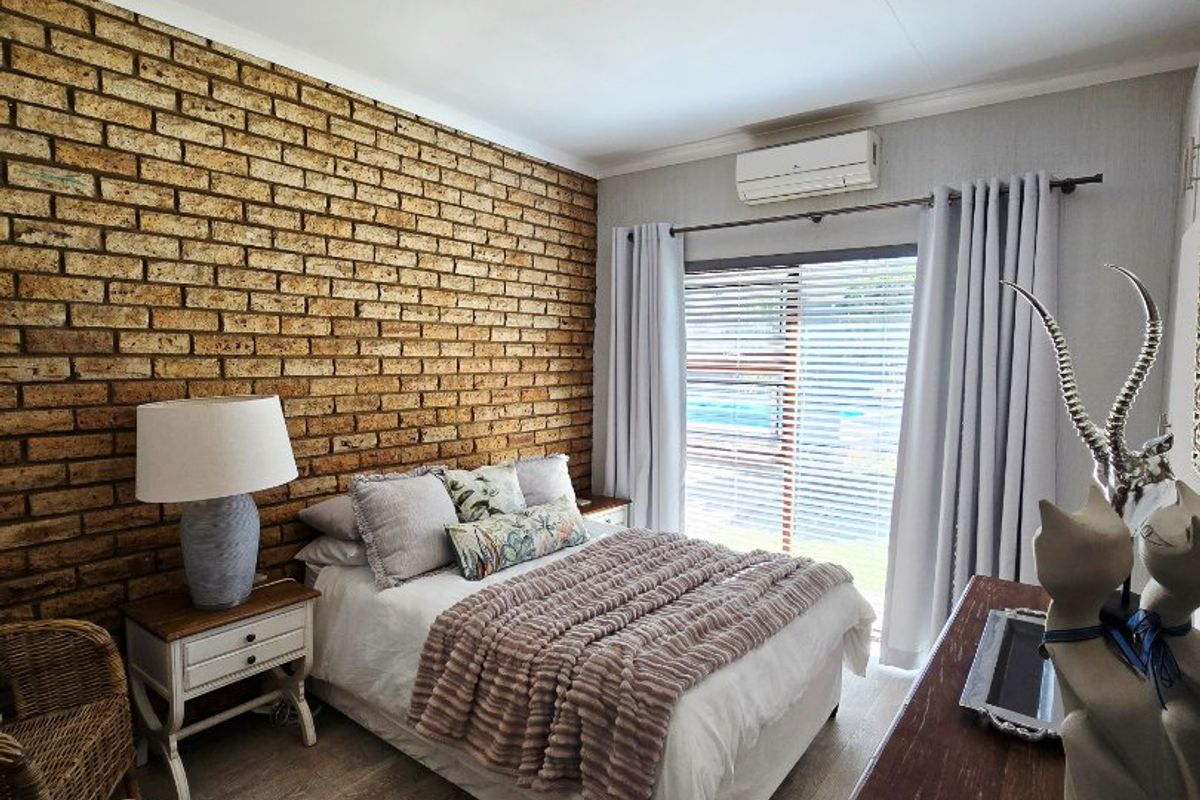 A well-maintained bedroom featuring an exposed brick accent wall, wood-look laminate flooring, and a split-system air conditioner with direct access to the outdoors.