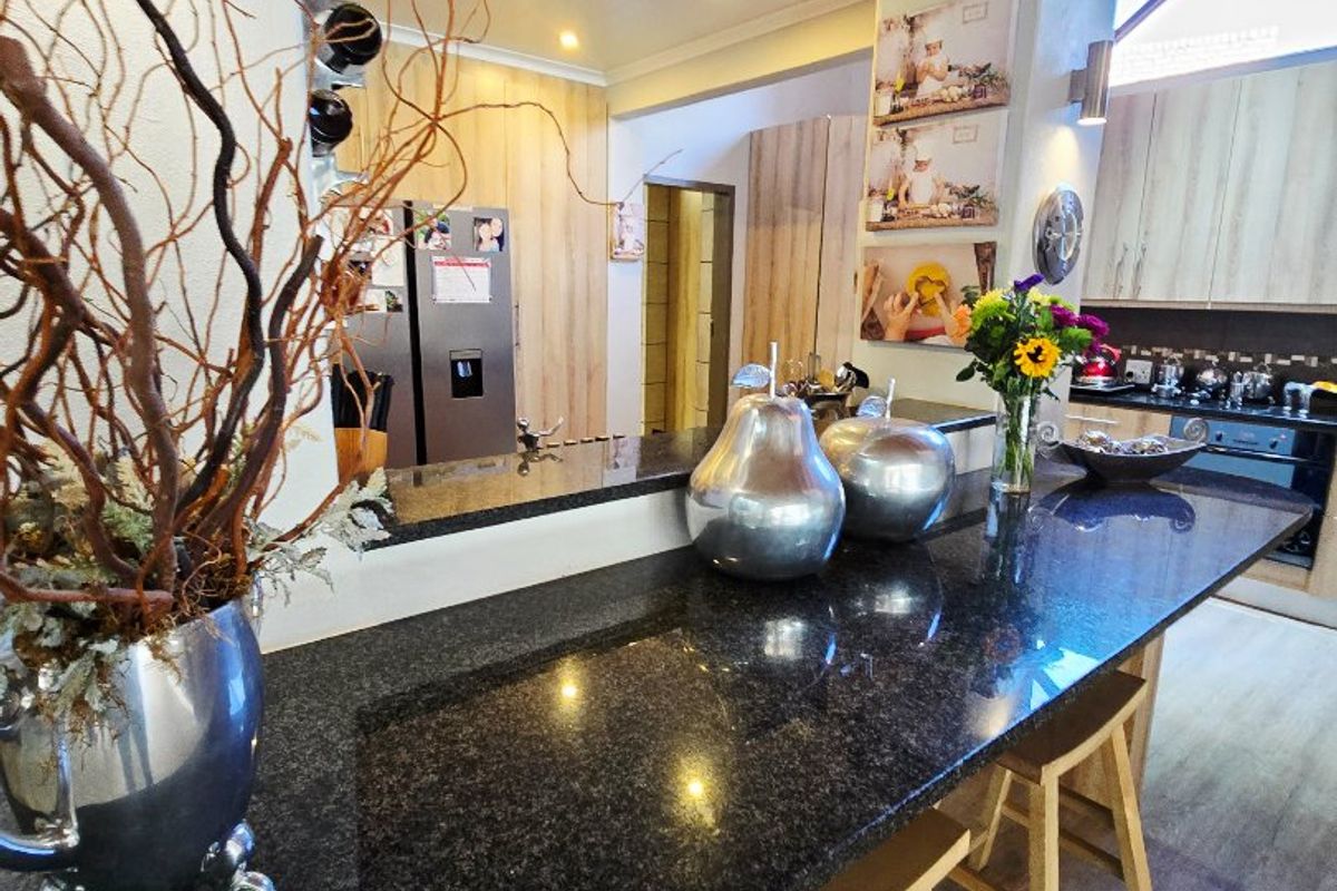 Modern kitchen featuring a spacious granite breakfast bar, light wood cabinetry, and high vaulted ceilings with recessed lighting.