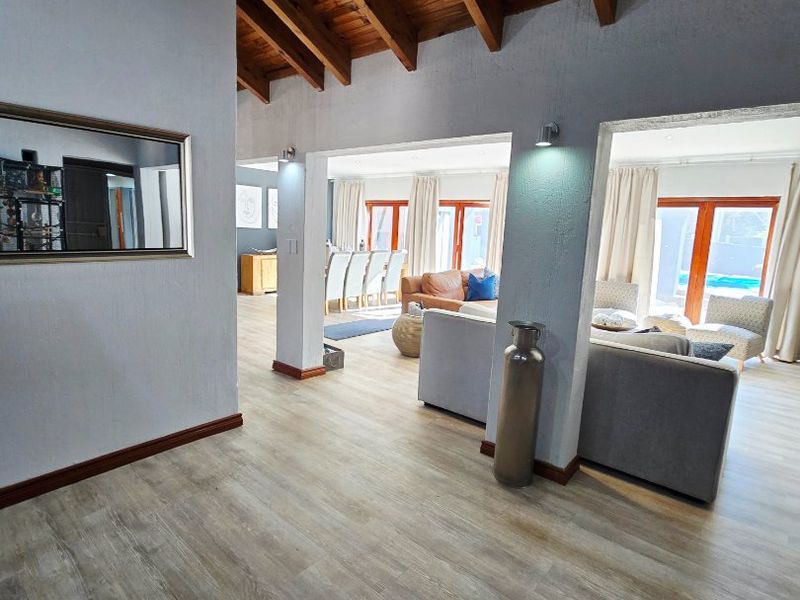 Spacious open-plan living area featuring exposed timber beam ceilings, modern laminate flooring, and seamless flow to the outdoor patio and pool area.