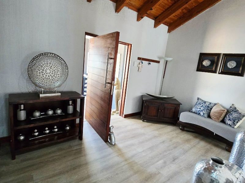A bright living area featuring vaulted ceilings with exposed timber beams and modern laminate flooring, leading to a solid timber entrance door.
