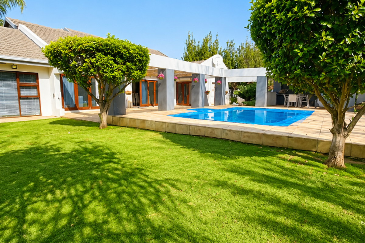 A well-maintained rear exterior featuring a swimming pool, tiled patio area with a pergola, and a spacious manicured lawn.