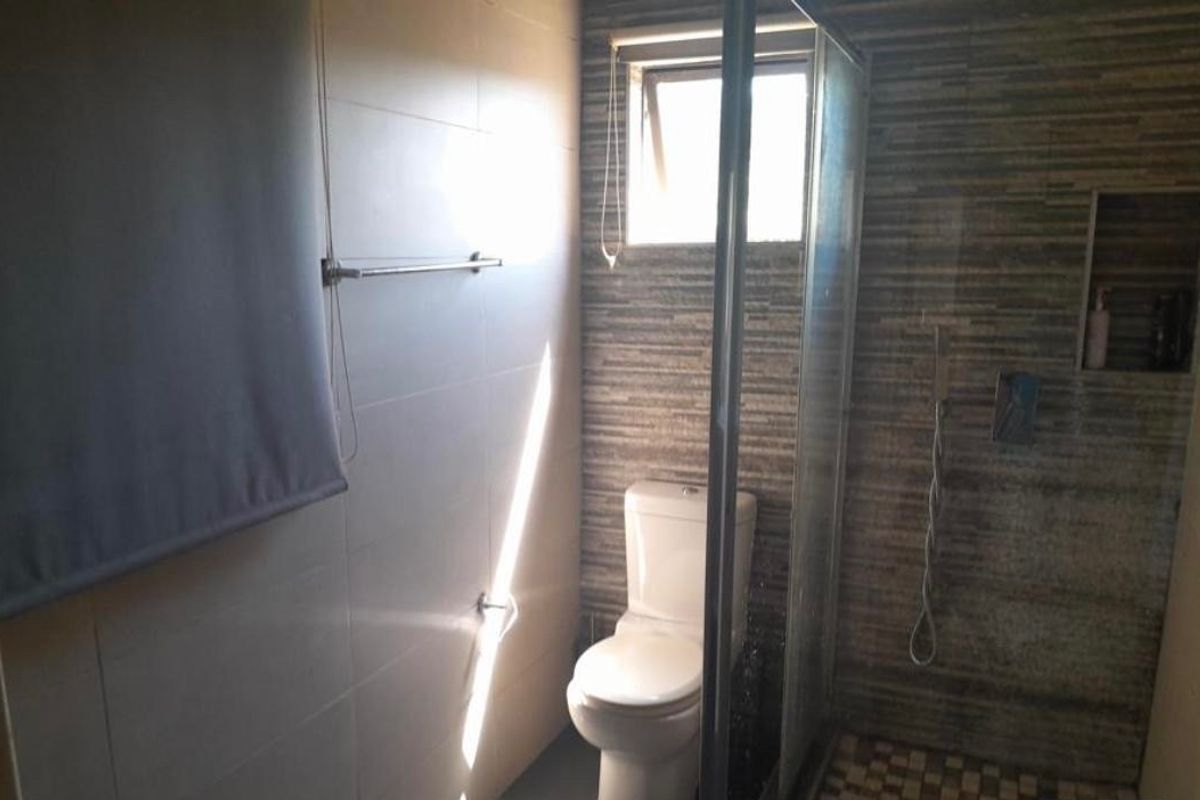 A functional bathroom featuring a glass-enclosed shower, modern toilet, and textured wall tiling with a built-in shower niche.