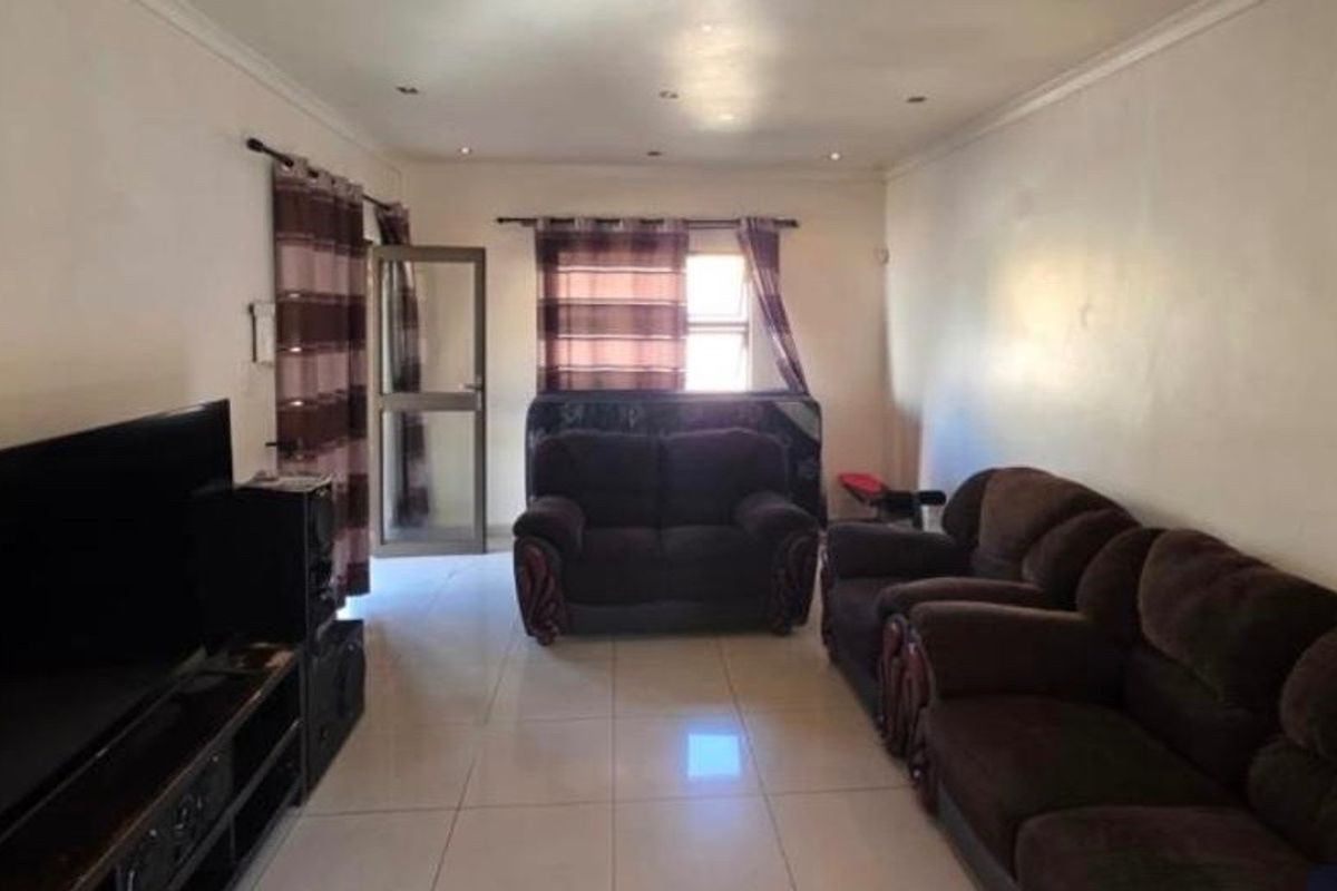 A spacious living room featuring tiled flooring, recessed ceiling lighting, and a glass-panelled door providing access to the exterior.