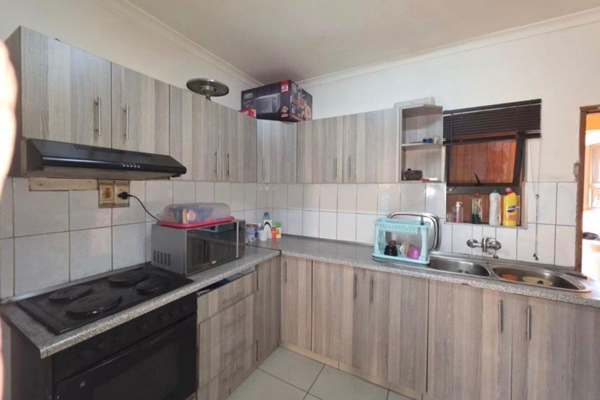 Functional kitchen featuring wood-look cabinetry, integrated electric oven and hob, extractor fan, and a double stainless steel sink with tiled splashback.