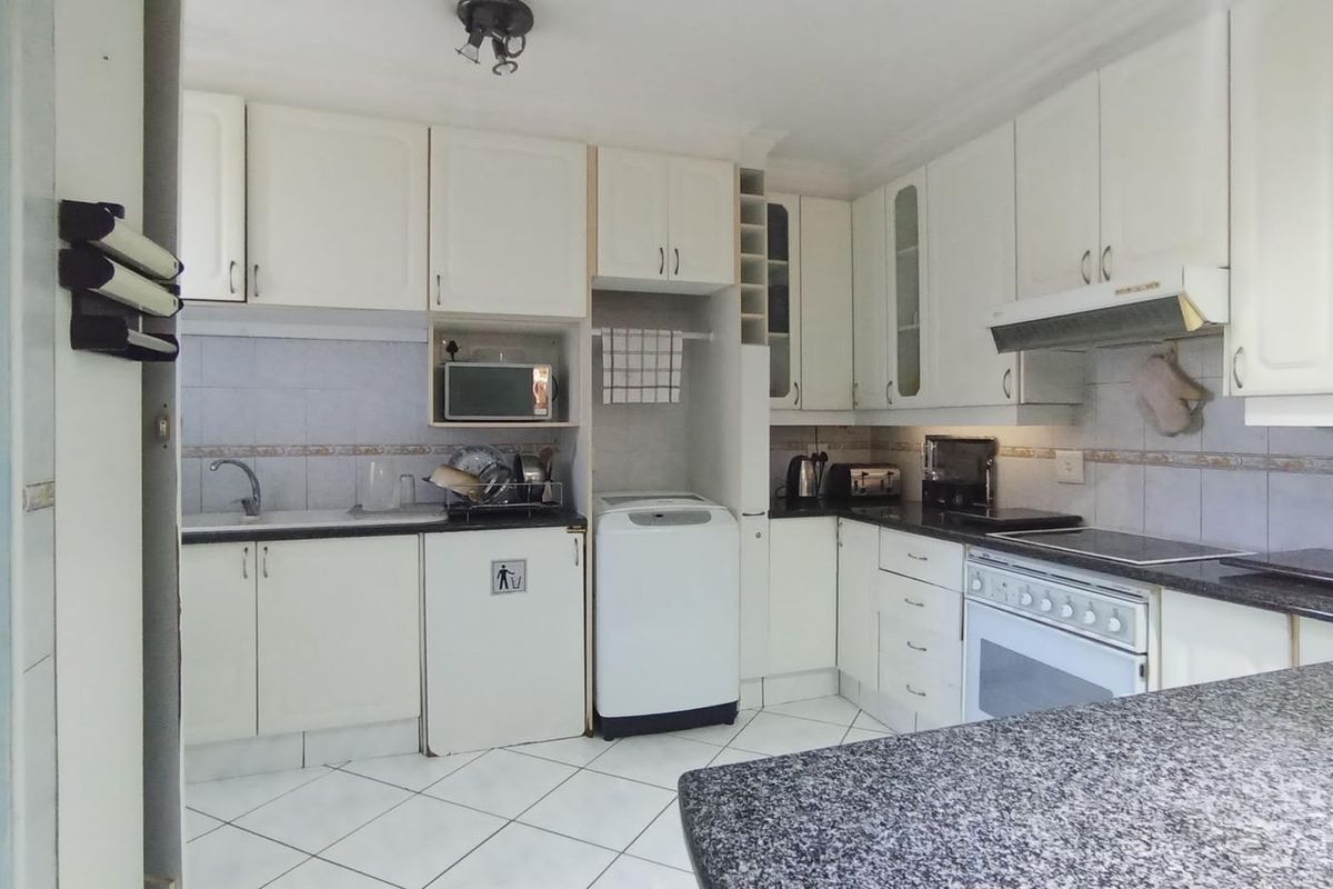 A functional kitchen featuring white cabinetry, granite-look countertops, tiled flooring, and a built-in oven with an extractor fan.