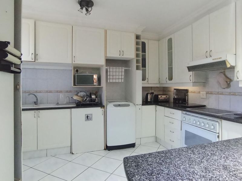 A functional kitchen featuring white cabinetry, granite-look countertops, tiled flooring, and a built-in oven with an extractor fan.