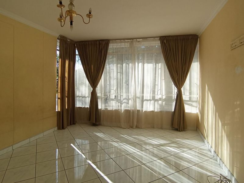A bright, empty living room featuring large windows with curtains and tiled flooring, offering a clean and versatile space for personalization.