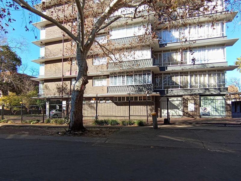 Street view of a multi-story apartment building featuring brick facade, metal security fencing, and balcony enclosures.