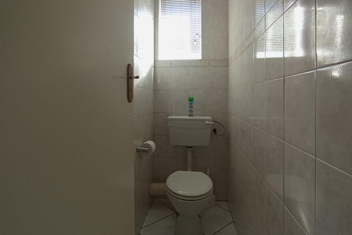 A compact guest toilet featuring full-height wall tiling, a standard ceramic toilet suite, and a small window for natural ventilation.