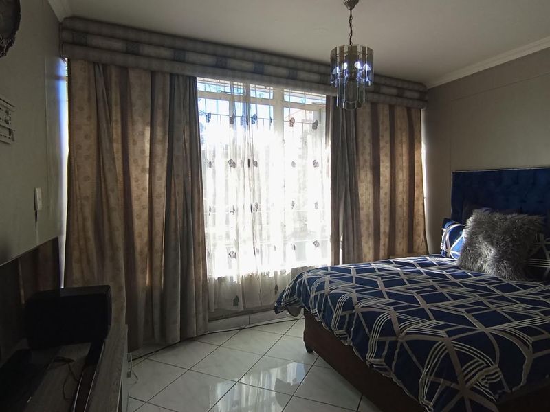 A bedroom featuring tiled flooring, a large window with curtain pelmet, and a central light fixture.