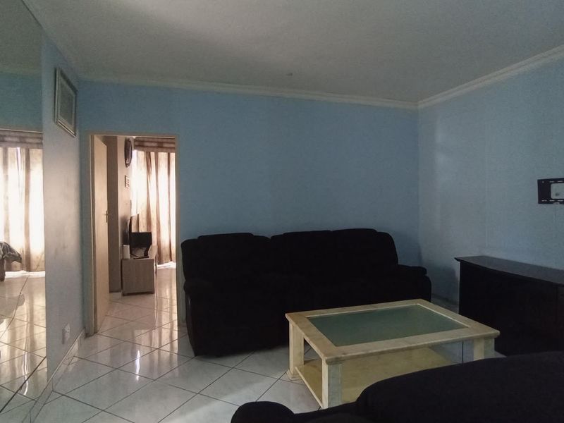 A living room featuring light blue walls, tiled flooring, and a doorway leading to an adjacent room.
