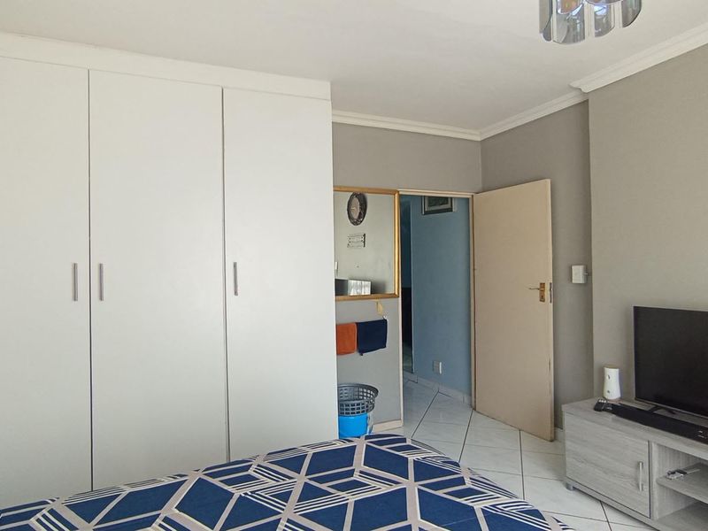A bedroom featuring built-in white wardrobes, tiled flooring, and neutral wall tones, providing a functional and well-lit living space.