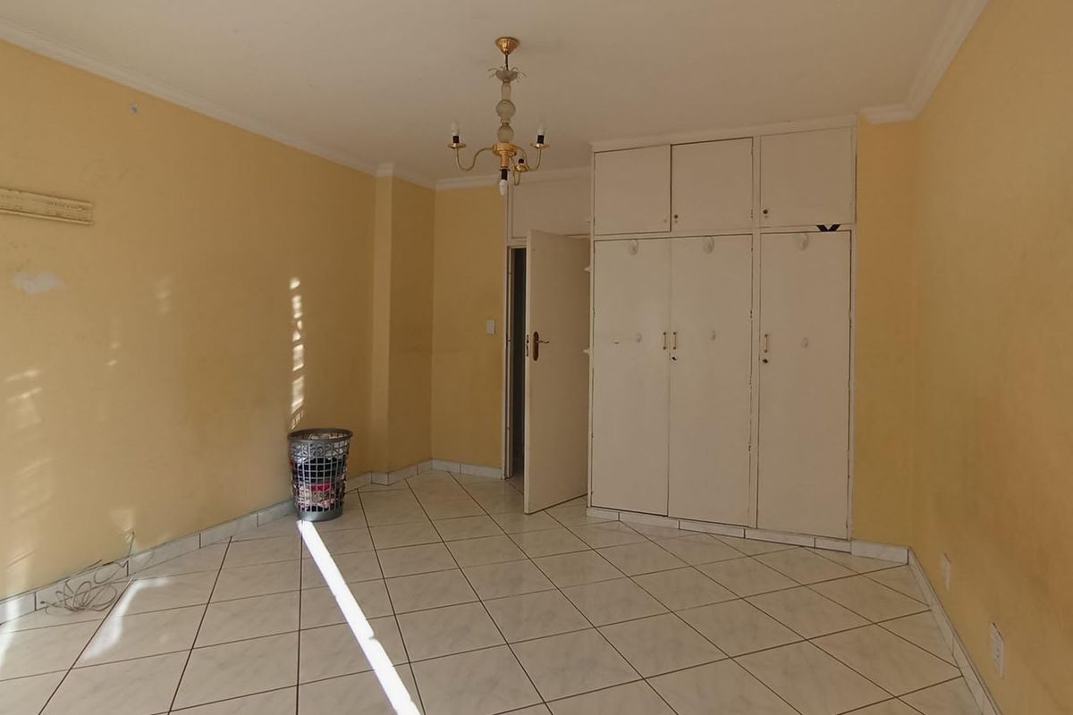 A vacant bedroom featuring built-in cupboards, tiled flooring, and a central light fixture, offering a blank canvas for renovation.