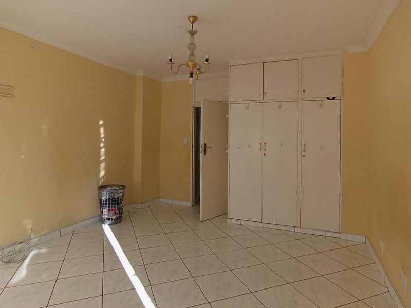 A vacant bedroom featuring built-in cupboards, tiled flooring, and a central light fixture, offering a blank canvas for renovation.