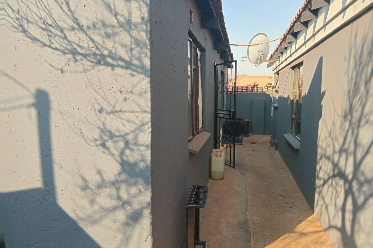 A narrow side passage between two exterior walls of the house, featuring security gates and a satellite dish mounted on the roofline.