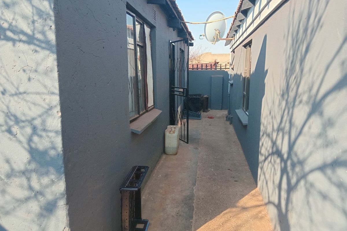 A narrow side passage between two exterior walls, featuring a concrete walkway, security gate, and satellite dish installation.