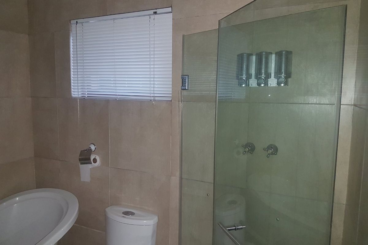 A functional bathroom featuring a glass-enclosed shower, a modern toilet, and neutral wall tiling with a window for natural light.