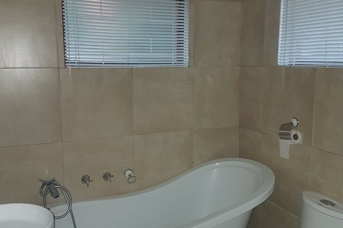 A bathroom featuring a freestanding clawfoot bathtub, a modern vessel sink, and a dual-flush toilet, finished with neutral wall and floor tiling.