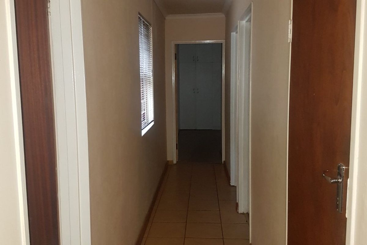 A functional interior hallway featuring tiled flooring, multiple wooden doors, and access to adjacent rooms.