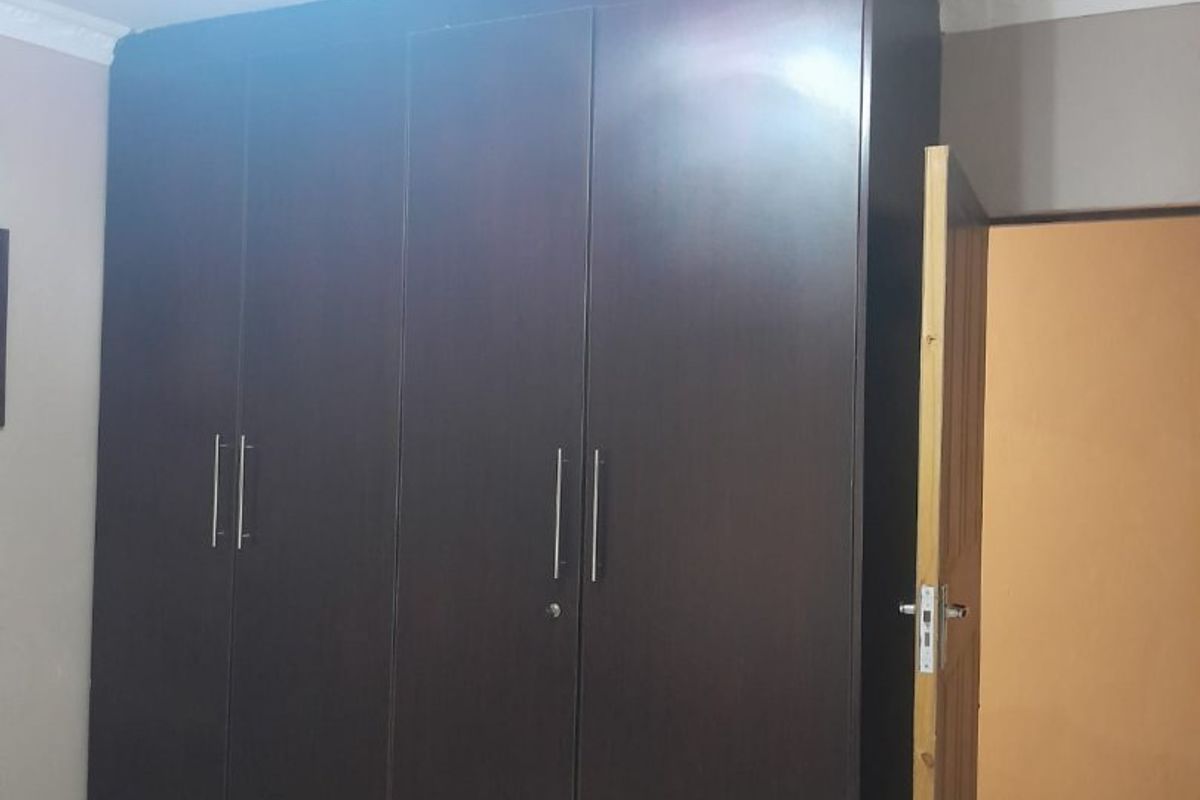 A bedroom featuring a large, dark wood built-in wardrobe with modern metal handles and tiled flooring.