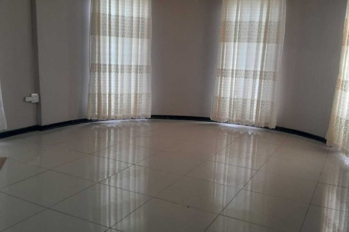 A spacious, empty living area featuring polished ceramic floor tiles, curved wall design, and large windows with fitted curtain tracks.