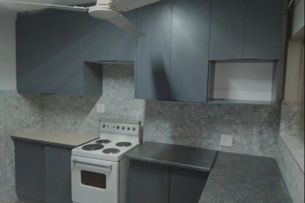 A functional kitchen featuring dark grey cabinetry, stone-look tiled splashbacks, granite-style countertops, and a freestanding electric stove.