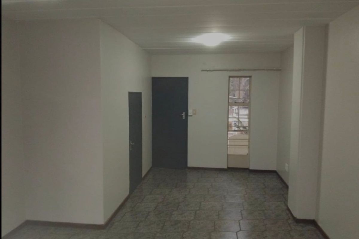 An empty, neutrally painted room featuring tiled flooring, a dark interior door, and a narrow window, offering a blank canvas for potential interior design.