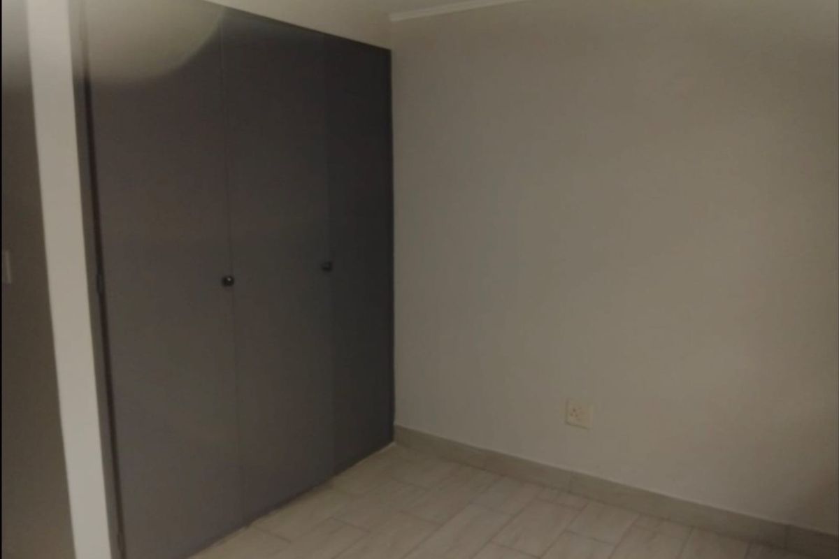 A clean, empty bedroom featuring built-in cupboards and neutral tiled flooring, providing a versatile space ready for personalization.