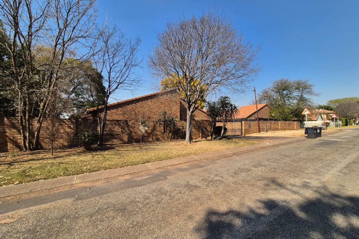 Street view of the property showing the brick boundary wall, driveway entrance, and established trees along the roadside.