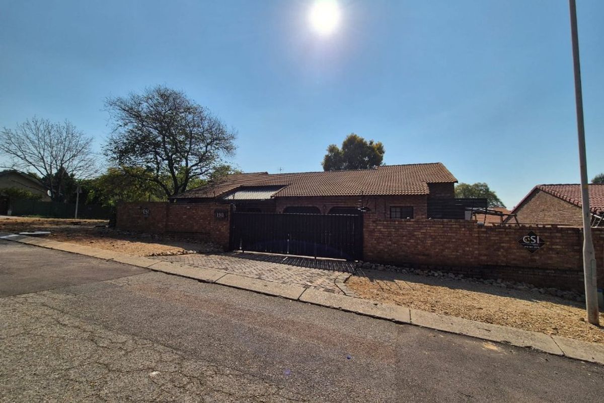 Street view of a single-story brick house featuring a tiled roof, perimeter wall, and a secure gated entrance.
