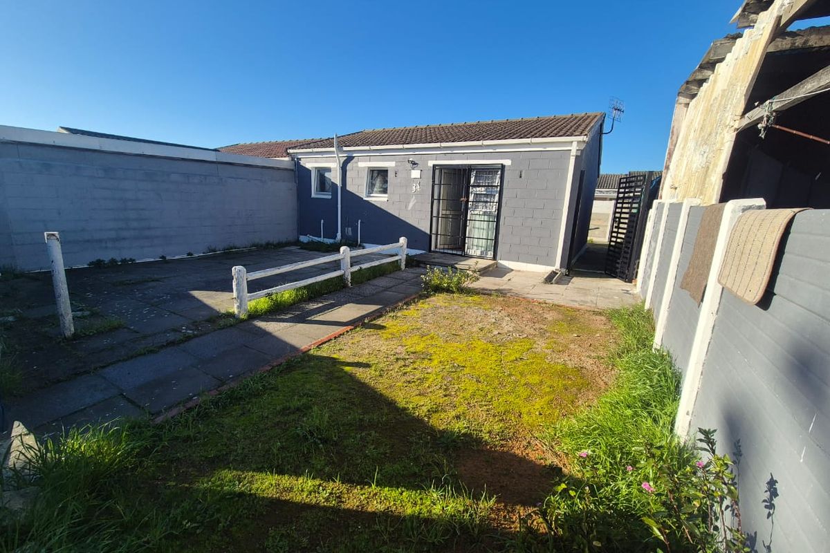 Rear view of the property featuring a paved patio area, a small lawn, and a secure gated entrance to the main dwelling.