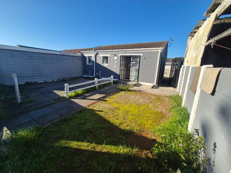 Rear view of the property featuring a paved patio area, a small lawn, and a secure gated entrance to the main dwelling.