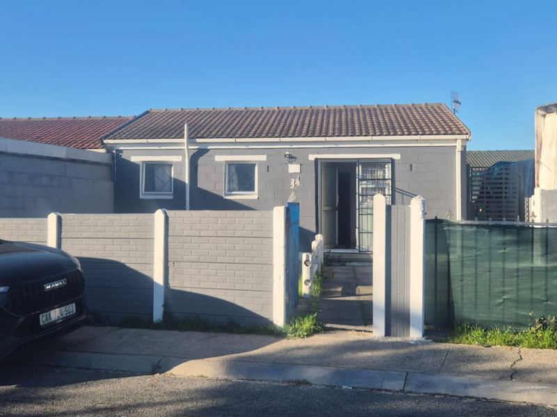 Front exterior view of a single-story house featuring a tiled roof, grey painted masonry walls, and a gated pedestrian entrance with a paved walkway.