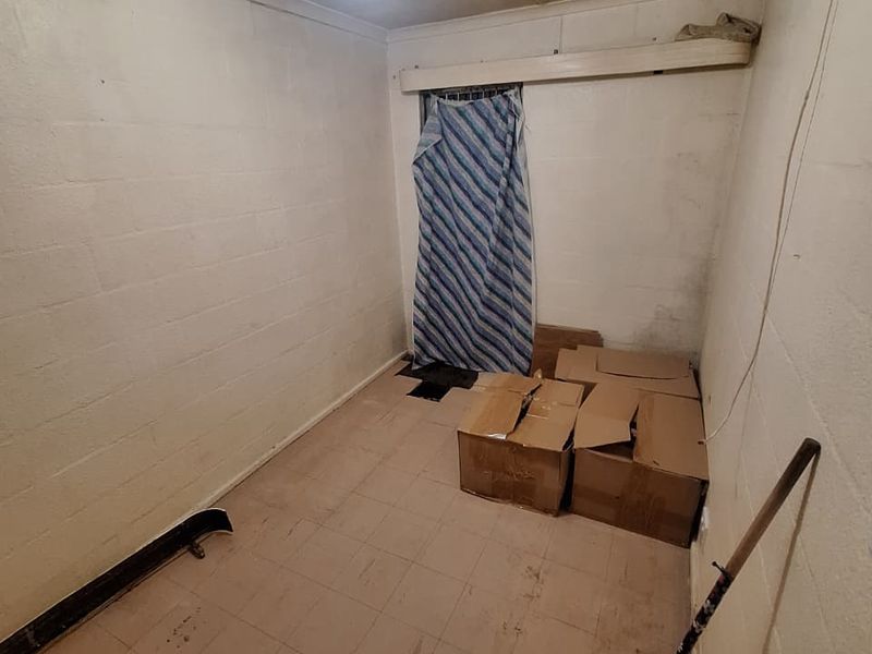 A small, utilitarian room featuring tiled flooring and painted block walls, currently used for storage and in need of cosmetic refurbishment.