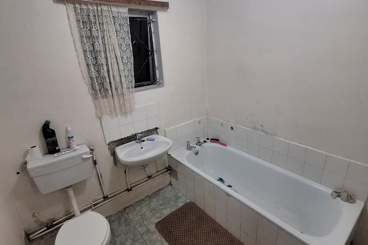 A dated bathroom featuring a standard bathtub, wall-mounted basin, and toilet with tiled flooring and visible wear on wall surfaces.