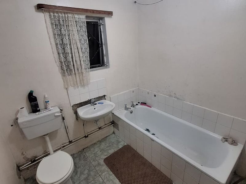A dated bathroom featuring a standard bathtub, wall-mounted basin, and toilet with tiled flooring and visible wear on wall surfaces.