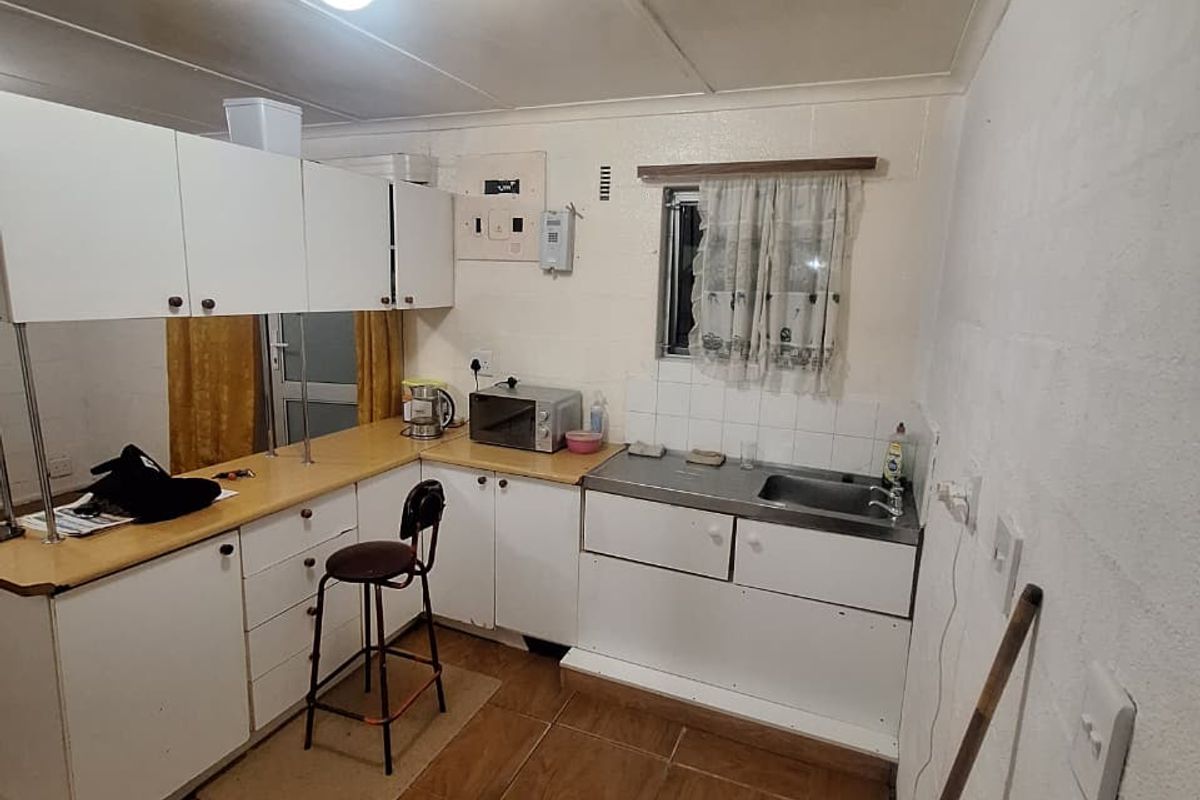 A compact kitchen featuring white cabinetry, laminate countertops, a stainless steel sink, and tiled flooring, offering a functional space with potential for modernization.