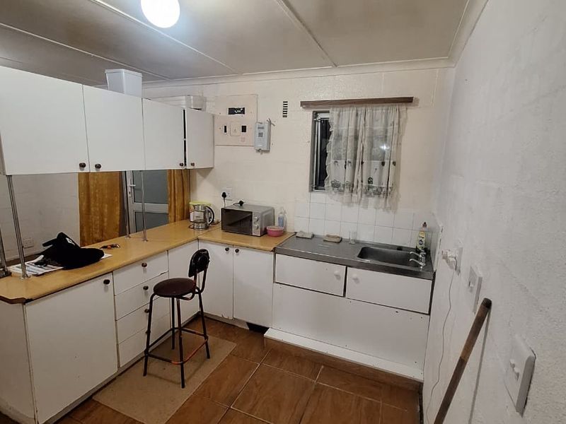 A compact kitchen featuring white cabinetry, laminate countertops, a stainless steel sink, and tiled flooring, offering a functional space with potential for modernization.