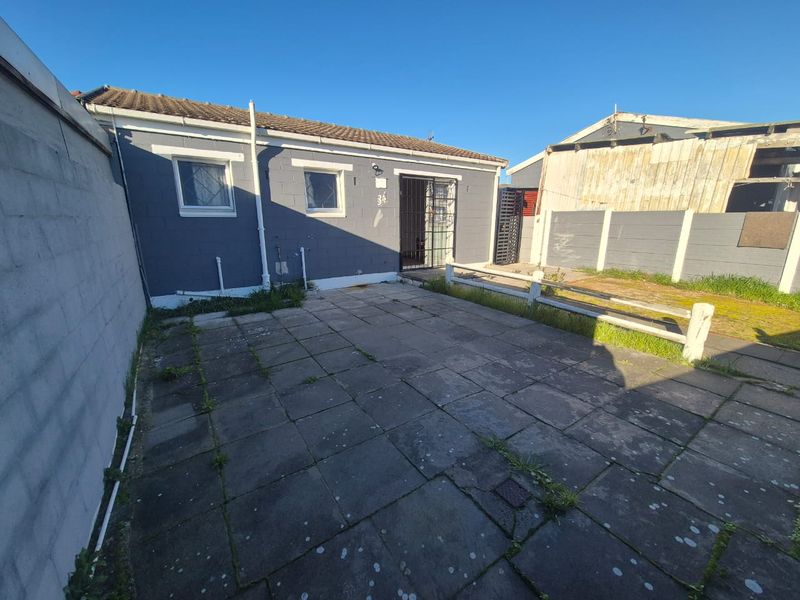 Rear exterior view of the property featuring a paved patio area, concrete block boundary walls, and a security gate entrance.