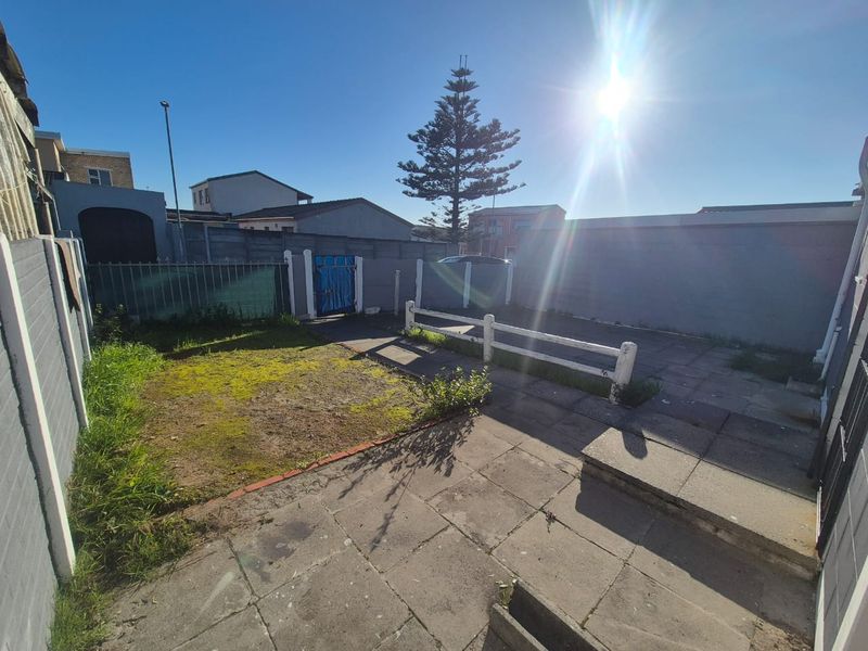 A rear outdoor area featuring paved sections, a small grass patch, and perimeter boundary walls with a gated access point.