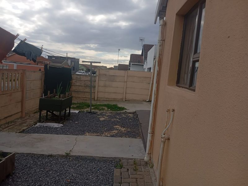 A rear exterior view of the property featuring a paved and gravel courtyard area, perimeter boundary walls, and external plumbing fixtures.