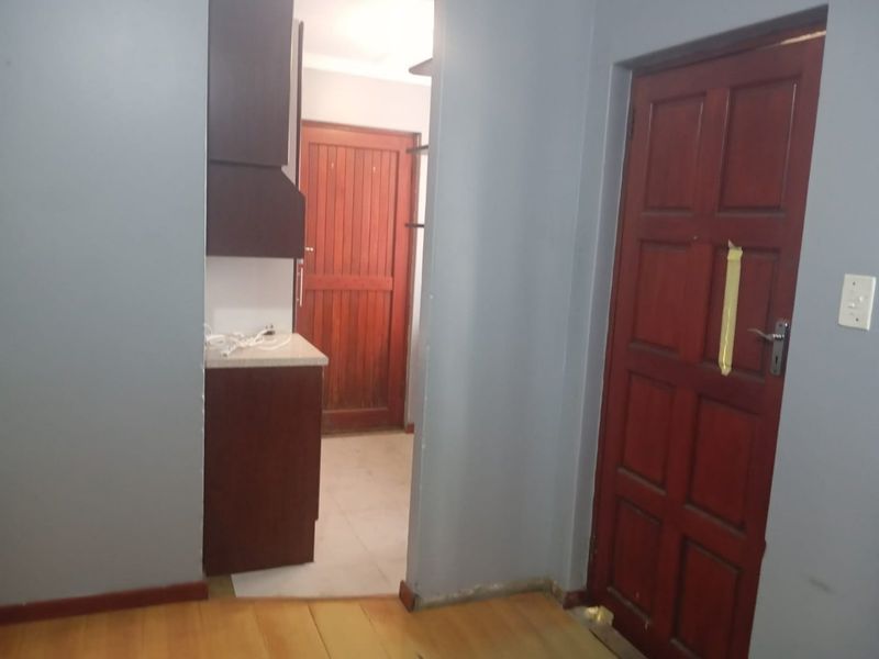 A view through a doorway into a kitchen area featuring dark wood cabinetry and a tiled floor, adjacent to a room with wooden flooring.