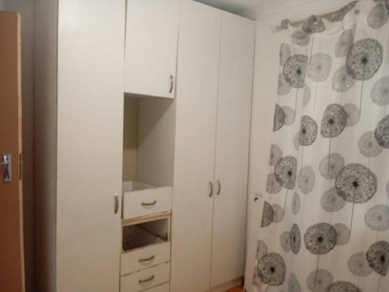 A bedroom featuring built-in white cabinetry with visible wear and missing drawer components, requiring maintenance or replacement.