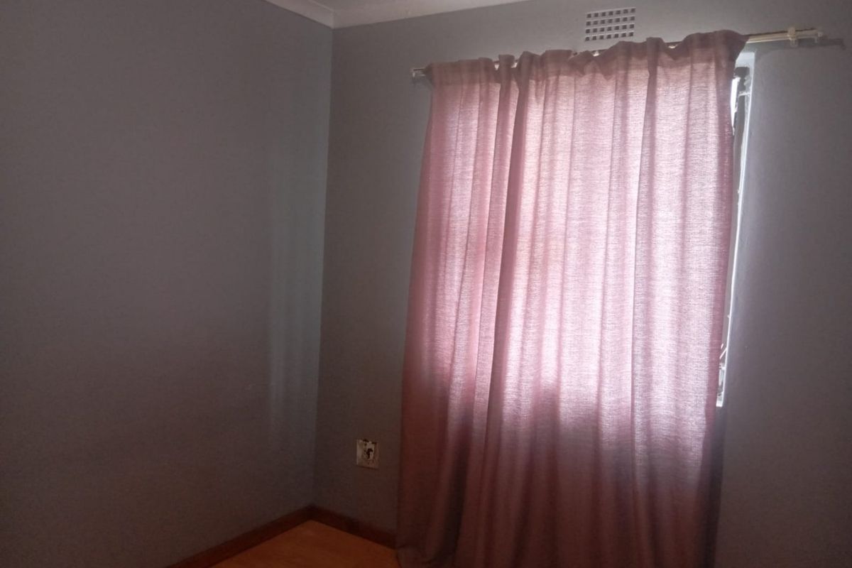 A simple, empty bedroom featuring laminate flooring, grey painted walls, and a window with a curtain rod.