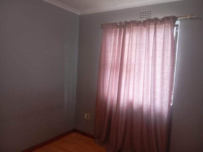 A simple, empty bedroom featuring laminate flooring, grey painted walls, and a window with a curtain rod.