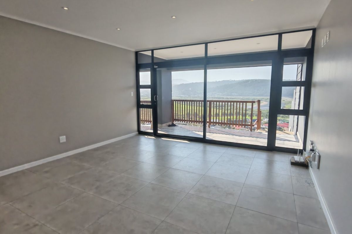 Spacious living area featuring large floor-to-ceiling glass sliding doors that open onto a balcony with scenic landscape views.