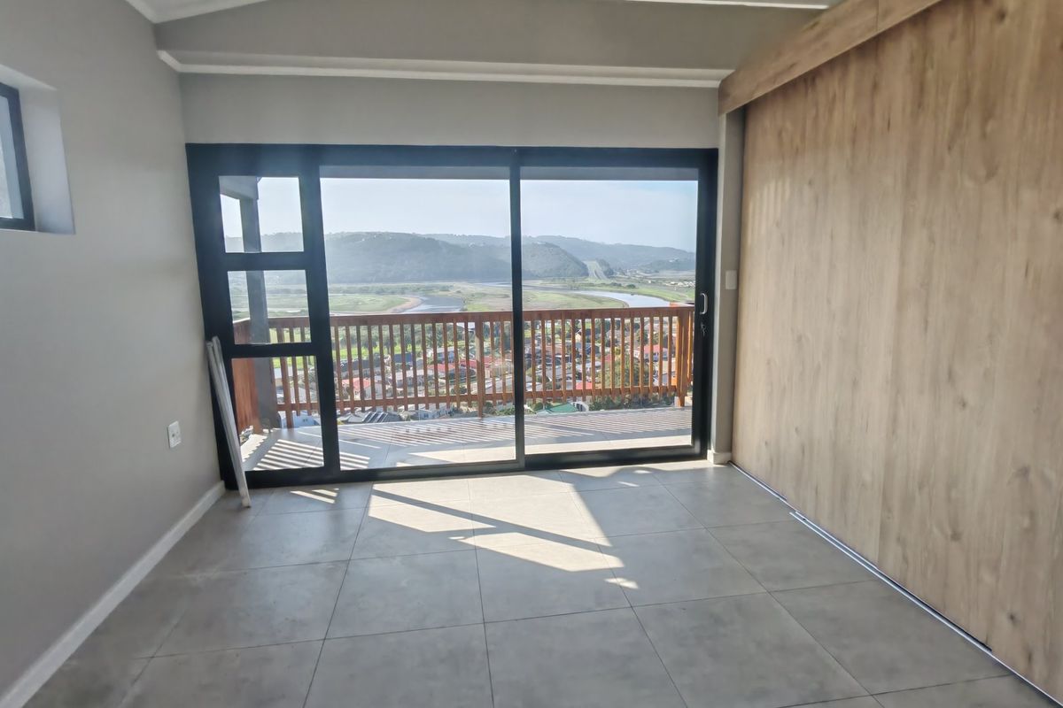 A bright bedroom featuring large sliding glass doors that open onto a balcony with scenic river and landscape views.