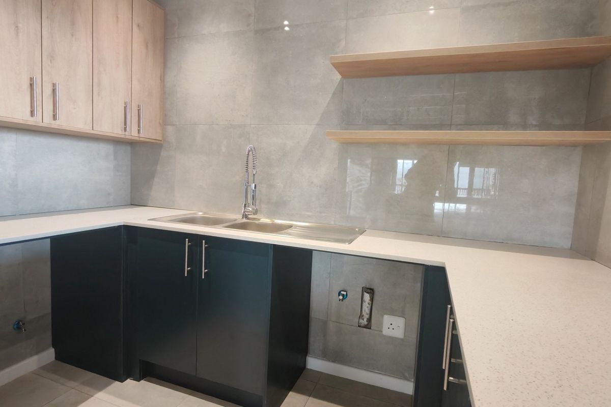 Modern kitchen featuring two-tone cabinetry, stone countertops, stainless steel sink with gooseneck faucet, and large format grey wall tiles with floating timber shelves.