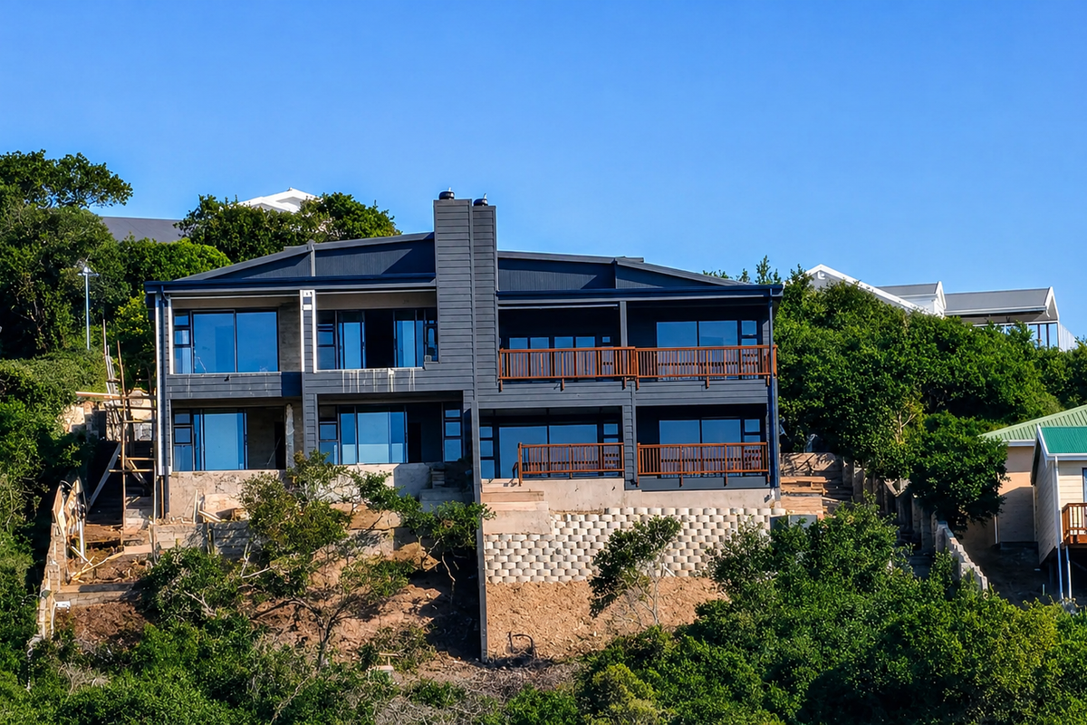 A modern multi-level residence featuring dark cladding, expansive glass sliding doors, timber balconies, and an unfinished terraced garden area.