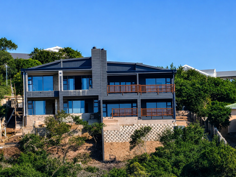 A modern multi-level residence featuring dark cladding, expansive glass sliding doors, timber balconies, and an unfinished terraced garden area.